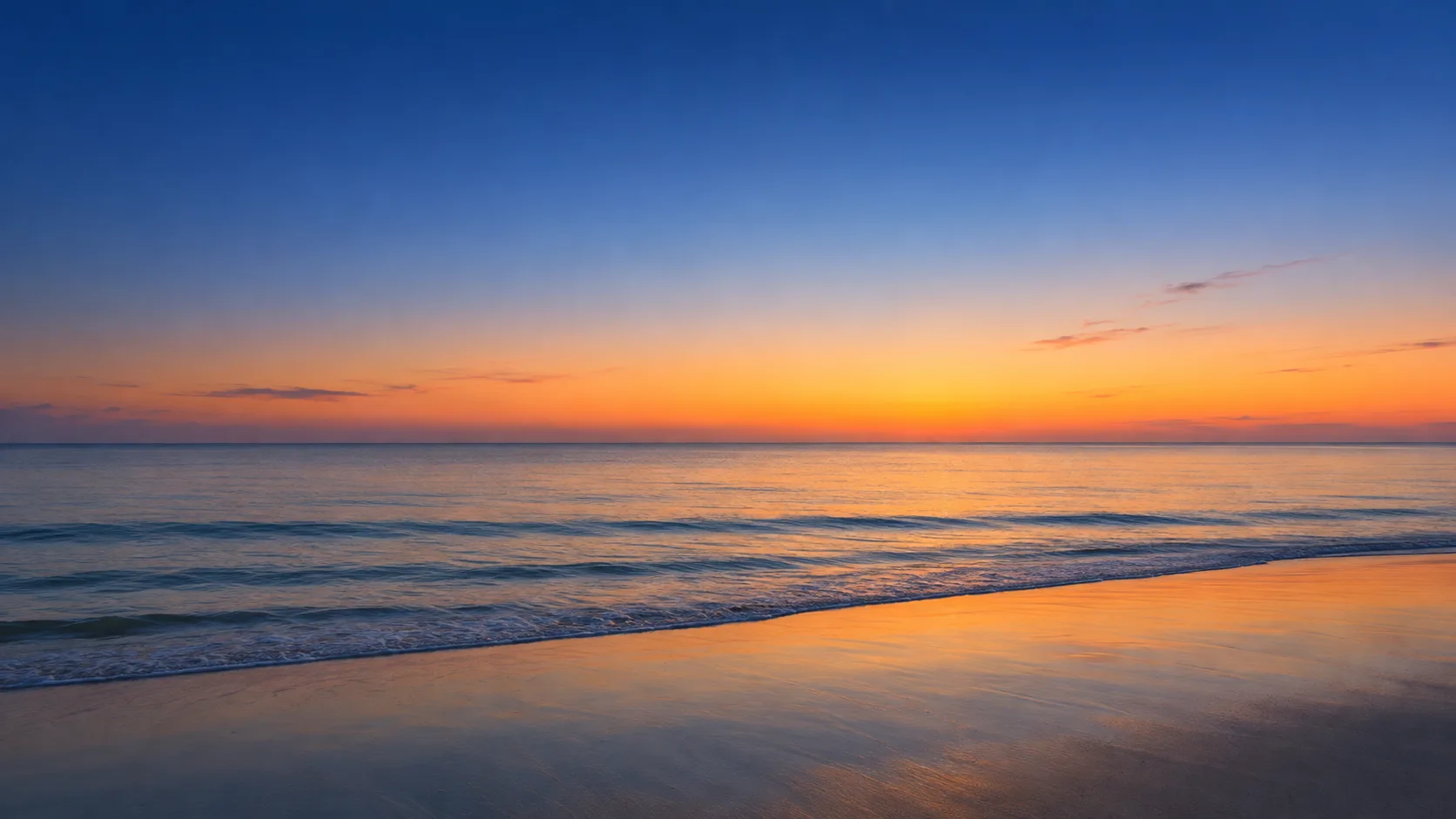 Calm Gulf shoreline at sunset with a glowing orange horizon